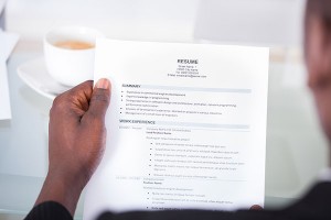 Person reviewing a resume with sections for summary and work experience, coffee cup in background, emphasizing tips for effective resume organization during National Resume Month.